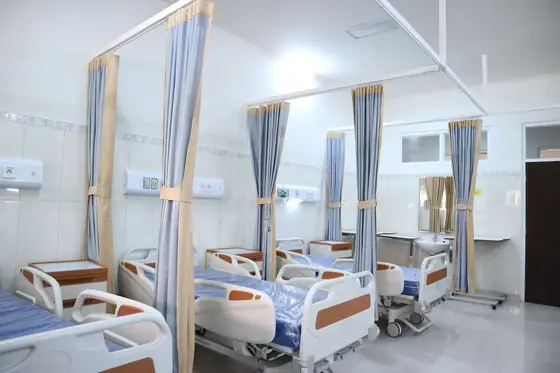 A hospital ward with several made-up beds separated by privacy curtains