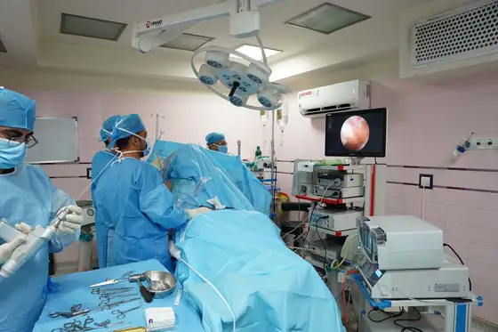 A surgical team at work in an operating room, with the endoscopic view shown on a wall-mounted screen