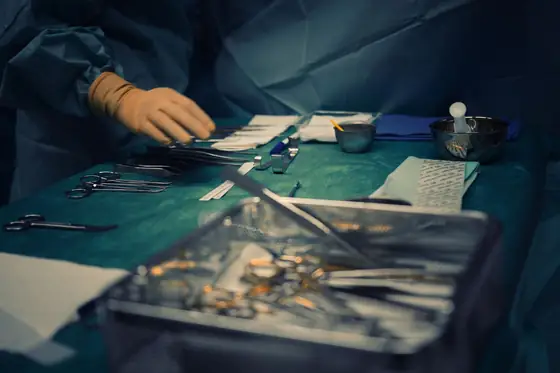 Surgical instruments laid out in rows on a sterile tray beside a draped operating field