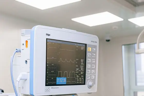 A vital signs monitor on a stand beside a prepared operating table