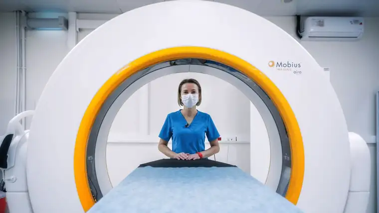 A nurse in scrubs standing at the opening of a large diagnostic scanner